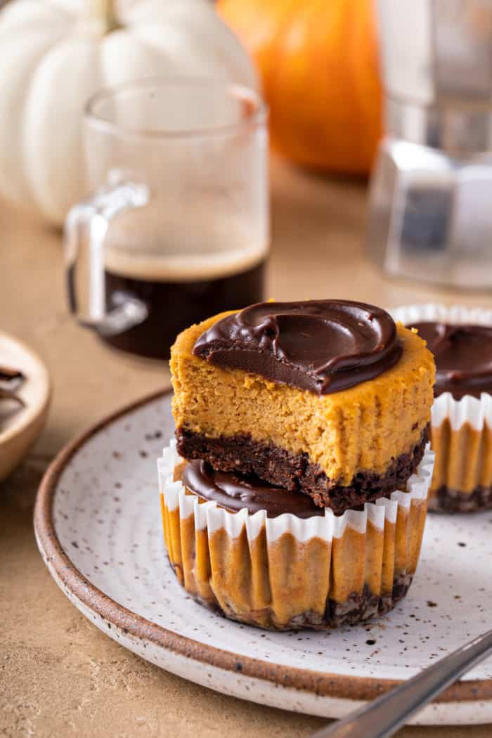 Two stacked mini pumpkin cheesecakes. The top one is unwrapped and has a bite taken out of it.