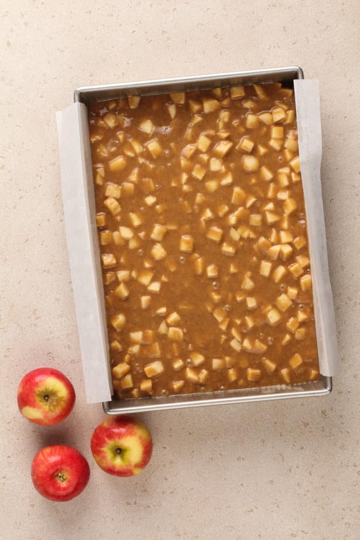 Unbaked caramel apple cake in a parchment-lined cake pan, ready to go in the oven.
