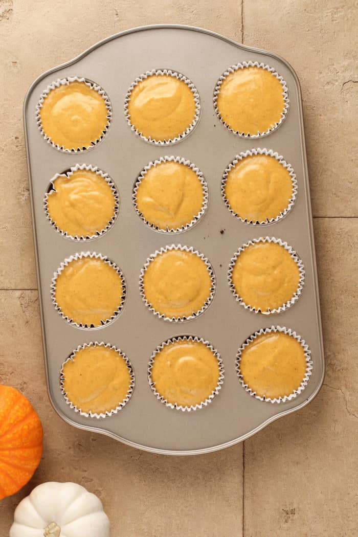 Unbaked mini pumpkin cheesecakes in a cupcake pan, ready to go in the oven.