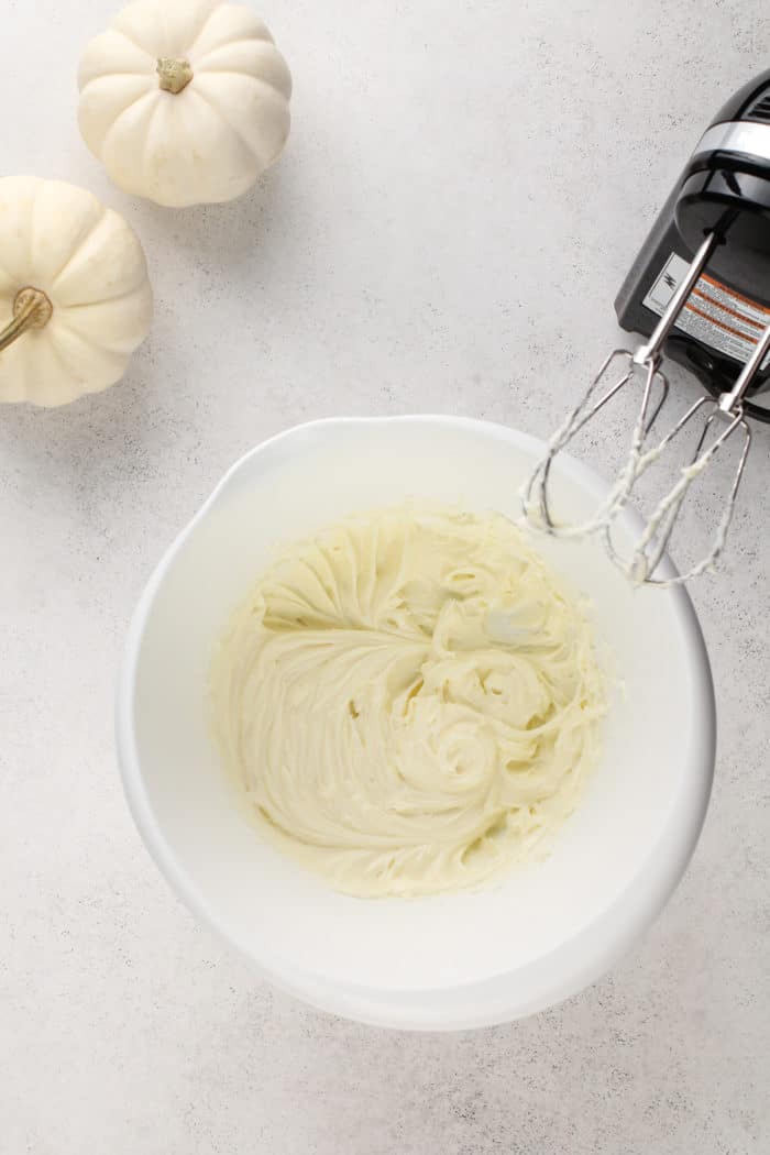 Cream cheese whipped with an electric mixer in a white mixing bowl.
