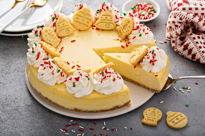 Sliced sugar cookie cheesecake on a gray counter surrounded by sugar cookies and sprinkles