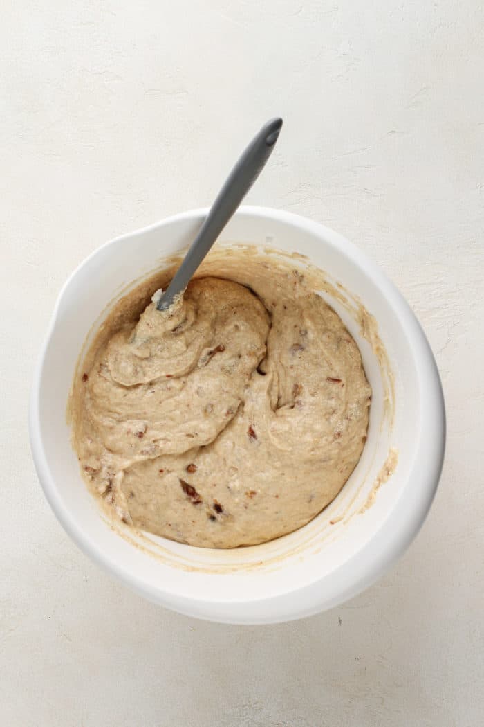 Date cake batter being stirred with a spatula in a white mixing bowl.