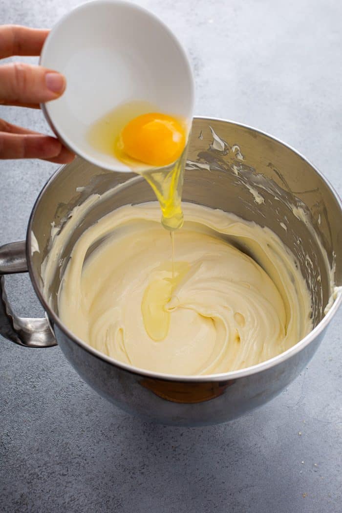Egg being added to cheesecake filling in a mixing bowl