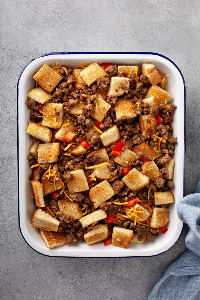 Overhead view of cubed bread, cooked sausage, and diced red pepper in a baking dish for breakfast casserole