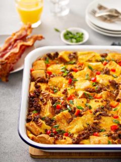 Casserole dish of make-ahead breakfast casserole on a gray counter with bacon and orange juice in the background