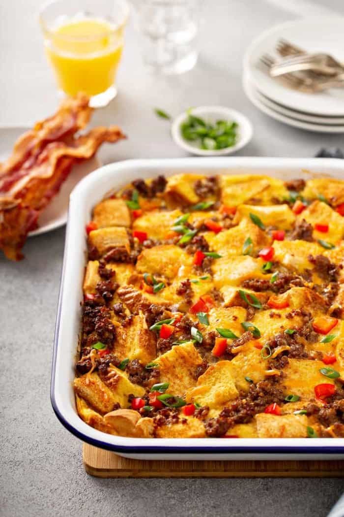 Casserole dish of make-ahead breakfast casserole on a gray counter with bacon and orange juice in the background