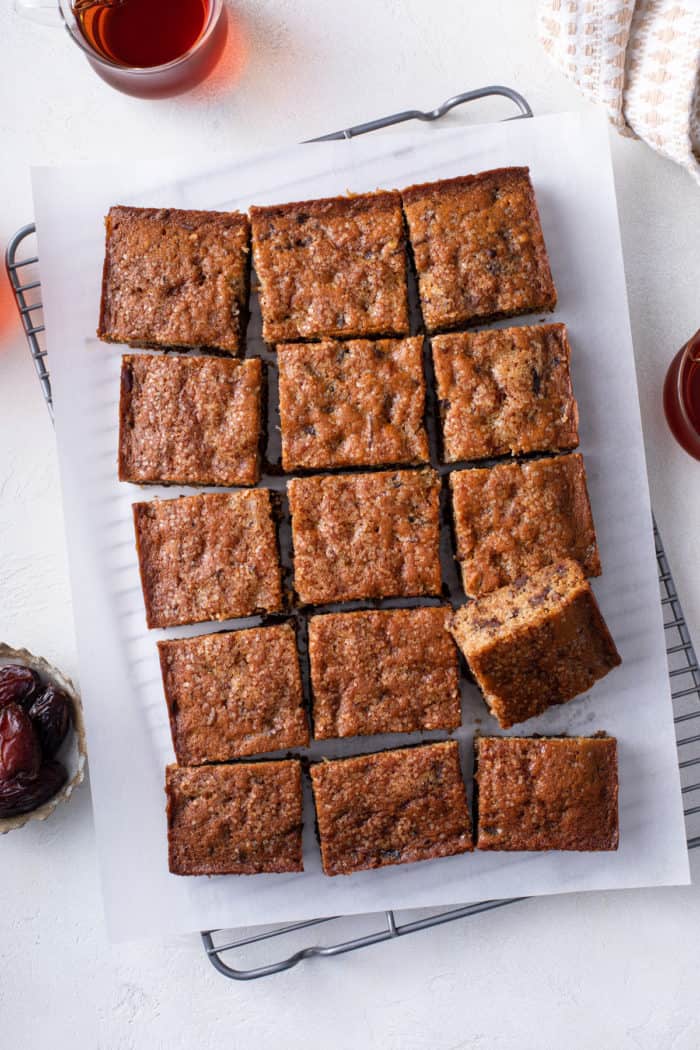 Overhead view of sliced date cake on a parchment-lined wire cooling rack.