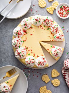 Overhead view of sliced sugar cookie cheesecake surrounded by white plates and sugar cookies