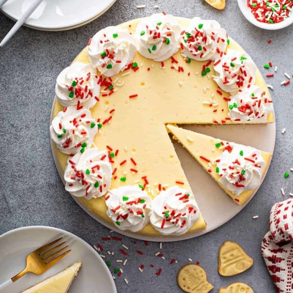 Overhead view of sliced sugar cookie cheesecake surrounded by white plates and sugar cookies