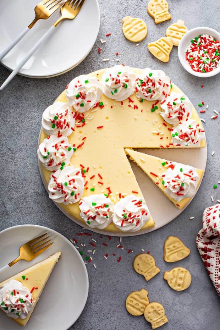 Overhead view of sliced sugar cookie cheesecake surrounded by white plates and sugar cookies