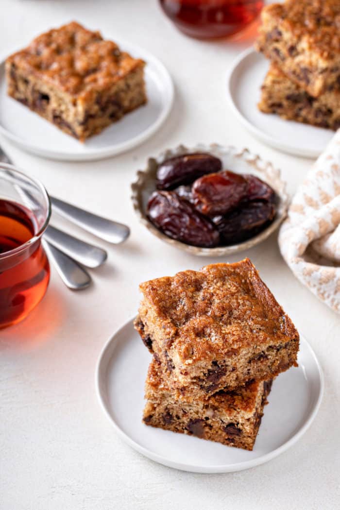 Two slices of date cake stacked on a white plate with more plates of cake visible in the background.