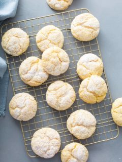 Gooey butter cookies scattered on a metal cooling rack on a gray counter