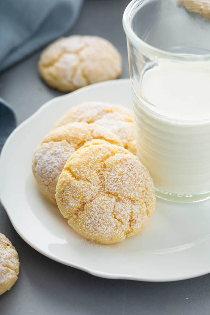 Three gooey butter cookies arranged next to a glass of milk on a white plate