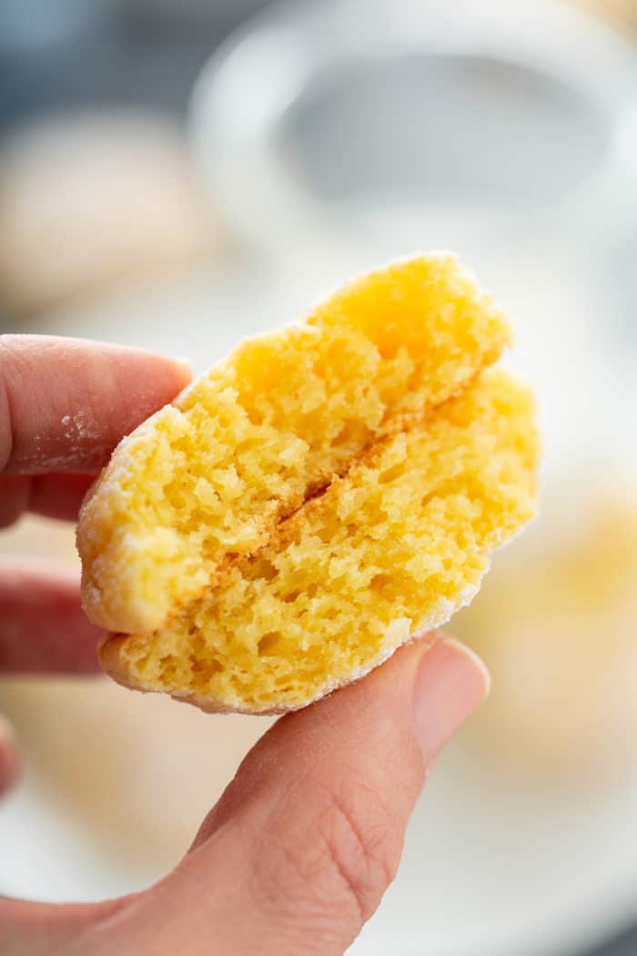 Hand holding up the two halves of a gooey butter cookie to the camera to show the cakey texture