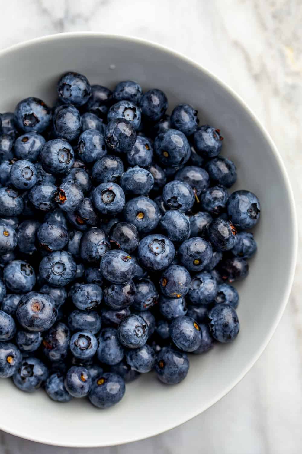 Fresh blueberries in a white bowl on a marble surface