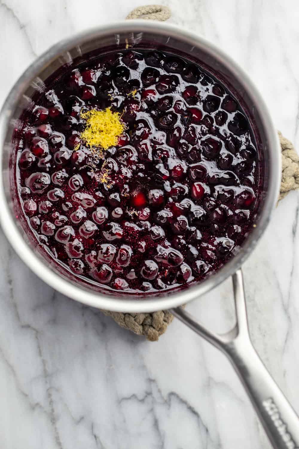 Lemon zest added to homemade blueberry sauce in a saucepan