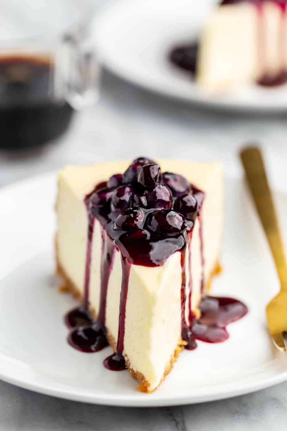 Slice of cheesecake topped with homemade blueberry sauce on a white plate with a gold fork