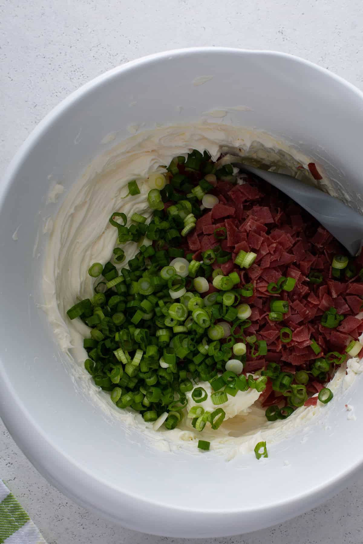 Chopped dried beef and sliced green onions added to cream cheese in a bowl.