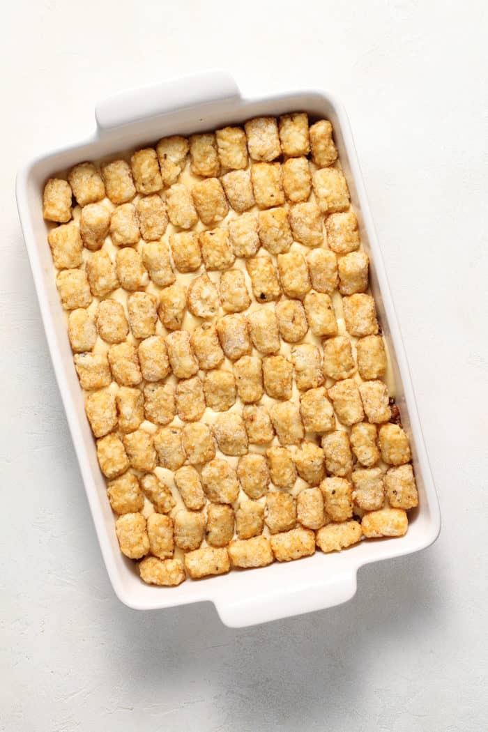 Assembled cheeseburger tater tot casserole in a white baking dish, ready to go in the oven