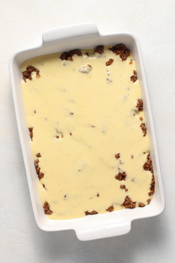 Cheese sauce poured over ground beef in a white casserole dish
