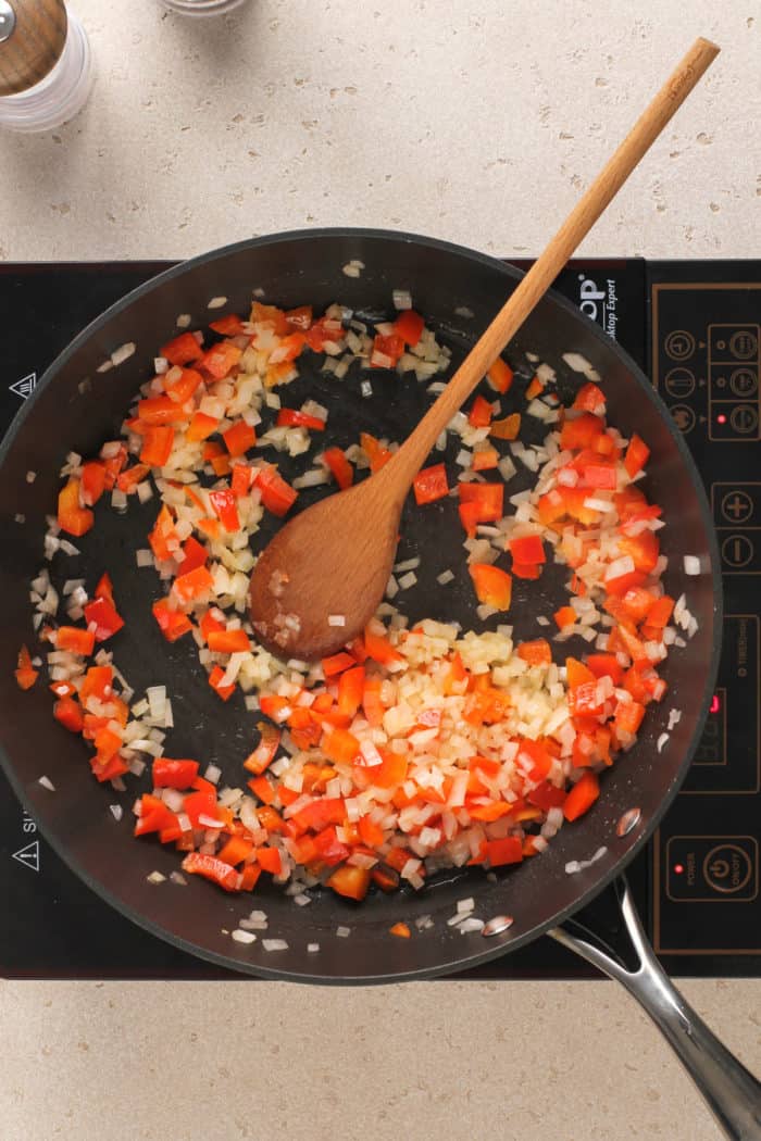 Onions and bell pepper being sauteed in a skillet.