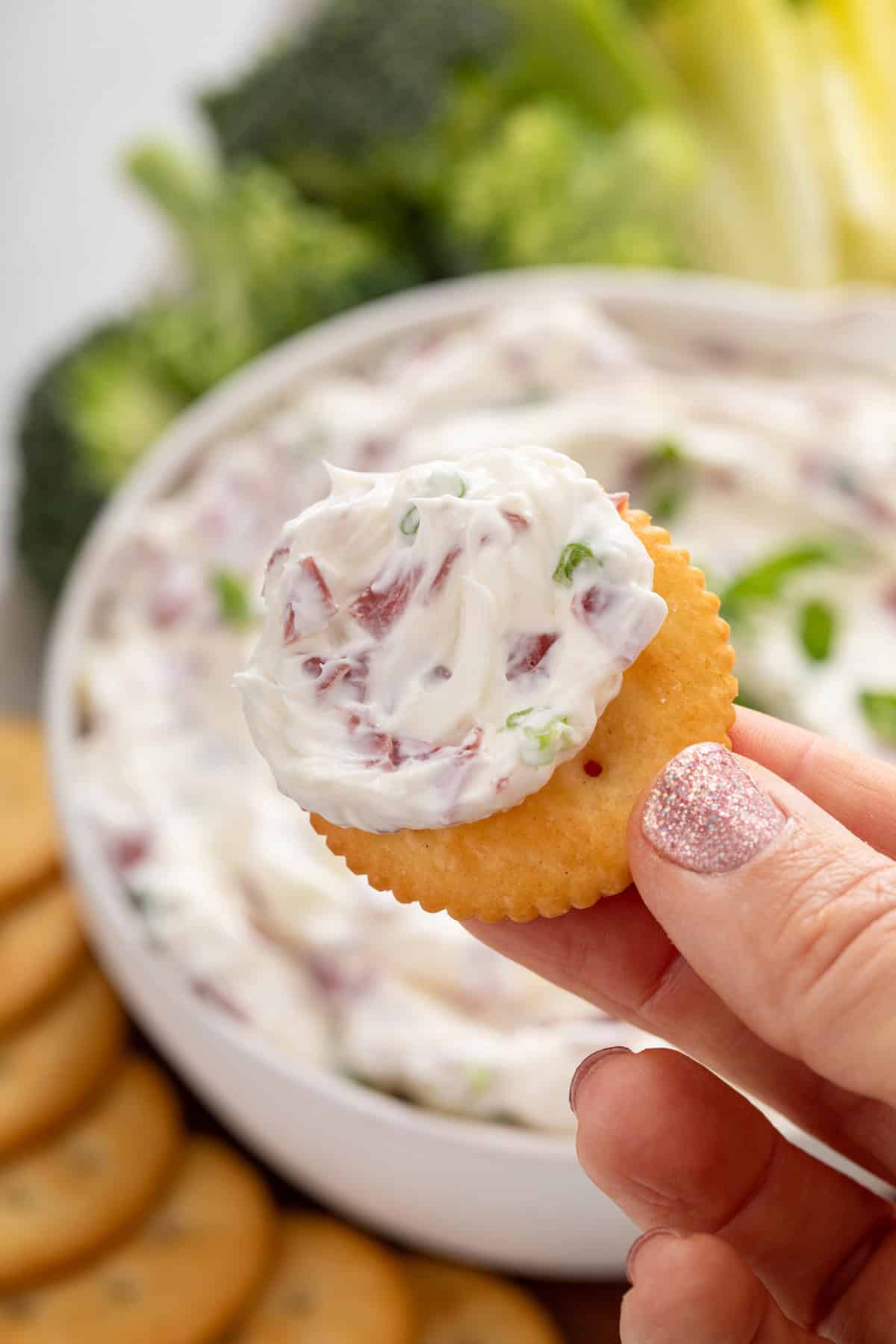 Hand holding up a cracker dipped in dried beef dip.