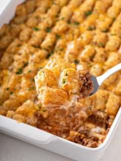 Spoon scooping a serving of cheeseburger tater tot casserole out of the baking dish