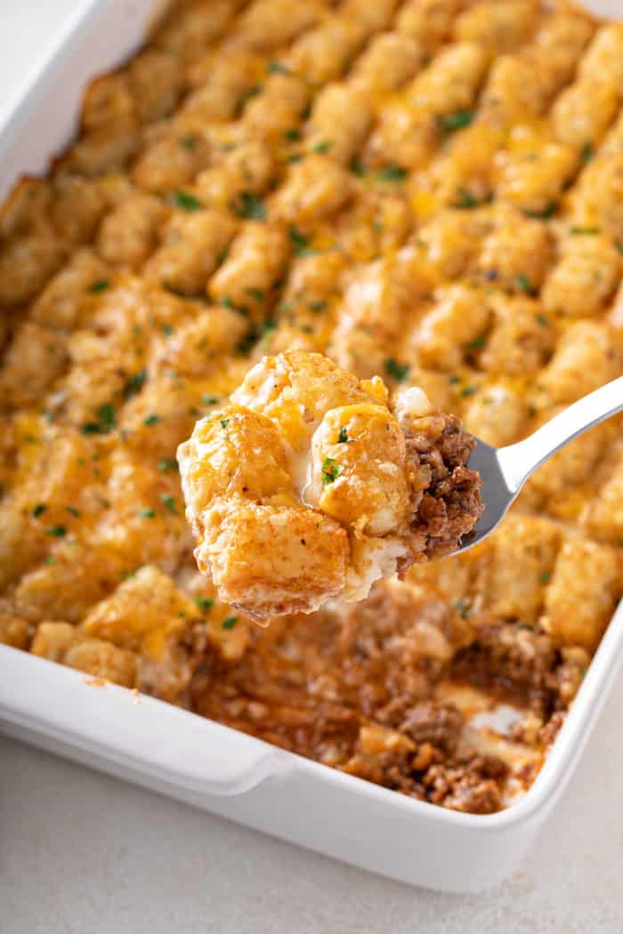 Spoon scooping a serving of cheeseburger tater tot casserole out of the baking dish