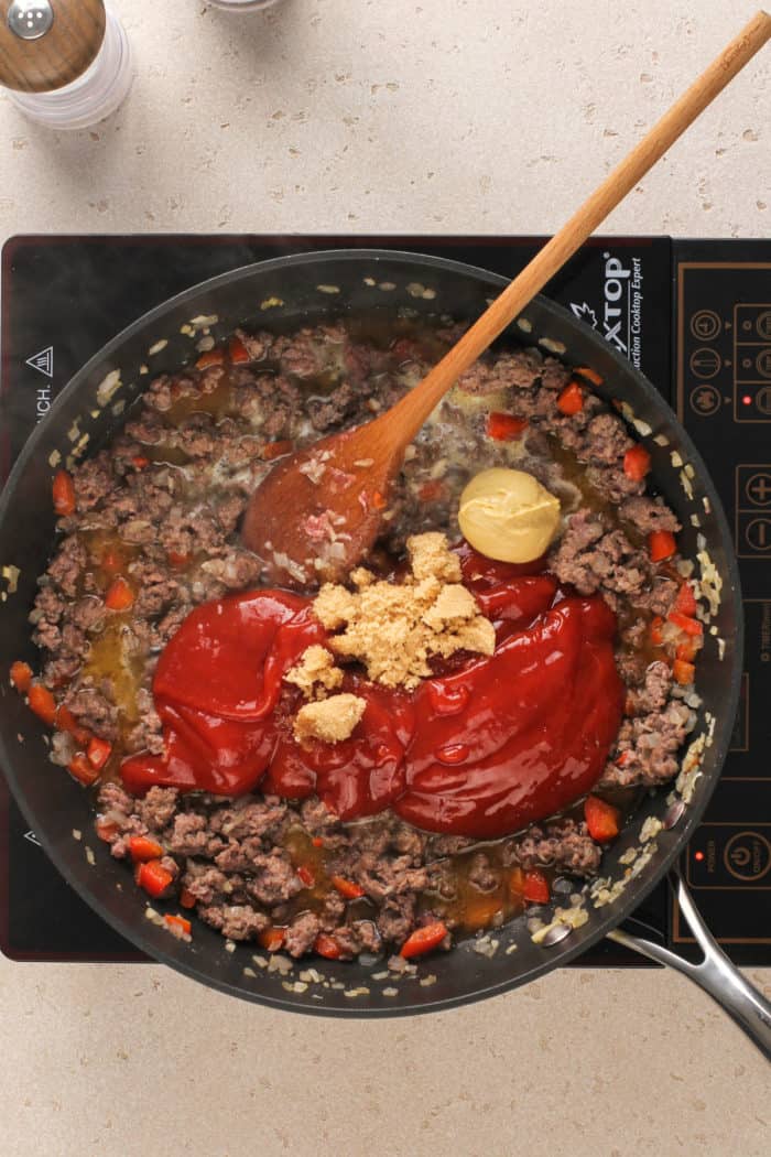 Ground beef with onions and bell pepper in a skillet with the rest of ingredients for sloppy joes.