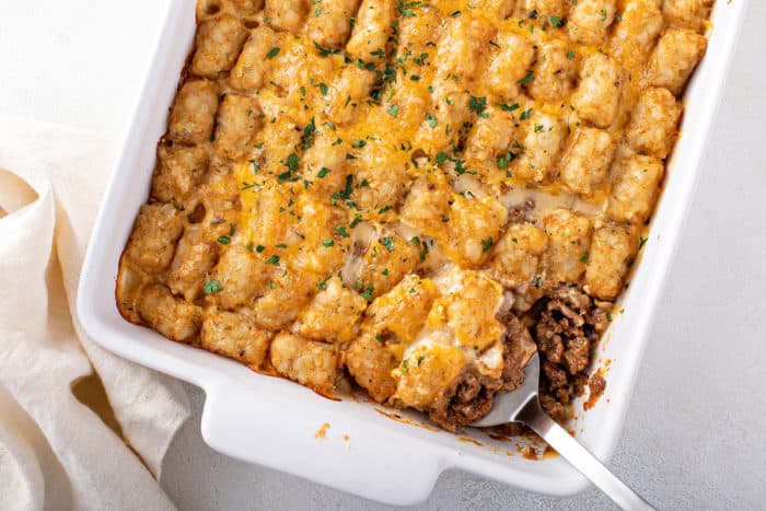 Cheeseburger tater tot casserole in a white baking dish, with a spoon in the corner of the casserole
