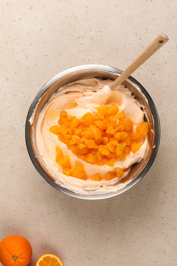 Chopped mandarin oranges being added to a bowl of orange fluff.