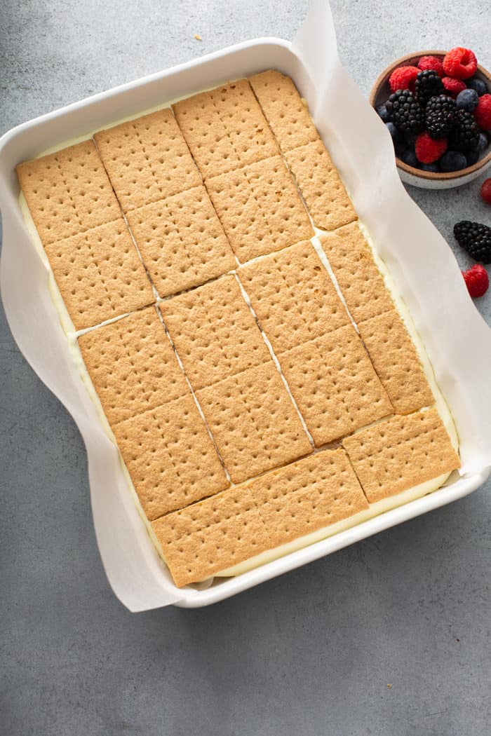 Layers of lemon icebox cake being assembled in a white baking dish