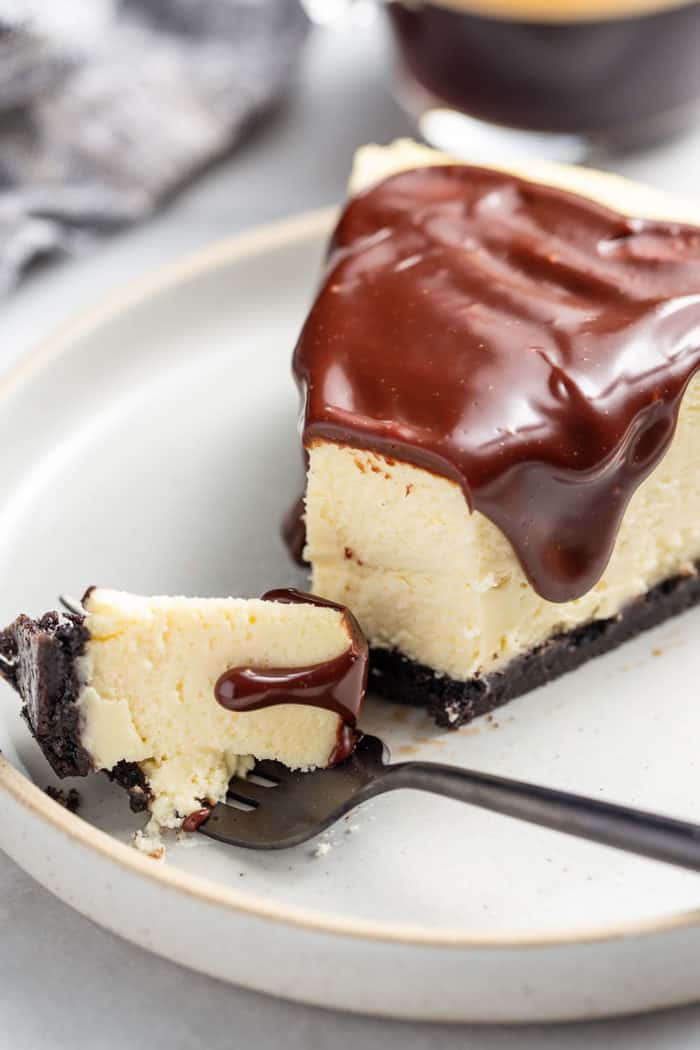 Fork with a bite of Baileys cheesecake laying on a plate next to a slice of the cheesecake