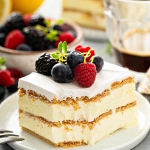 Slice of lemon icebox cake with a bite taken out of the corner, plated on a white plate and topped with fresh berries