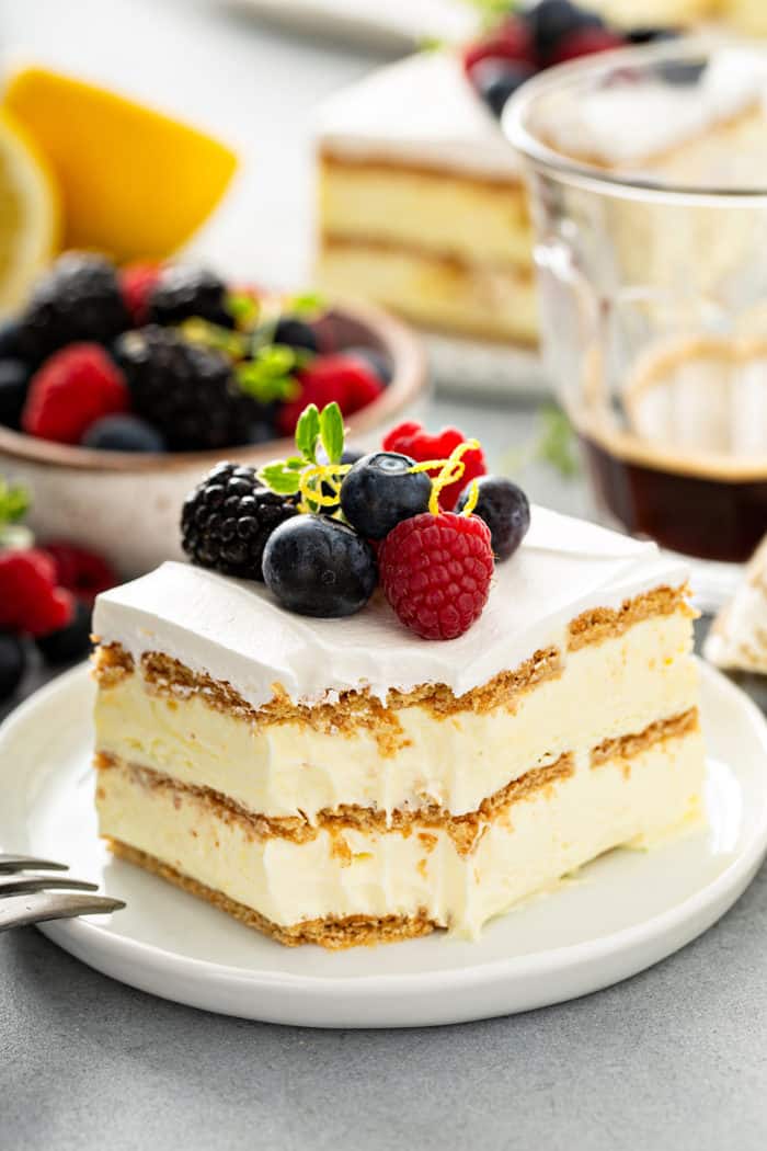 Slice of lemon icebox cake with a bite taken out of the corner, plated on a white plate and topped with fresh berries