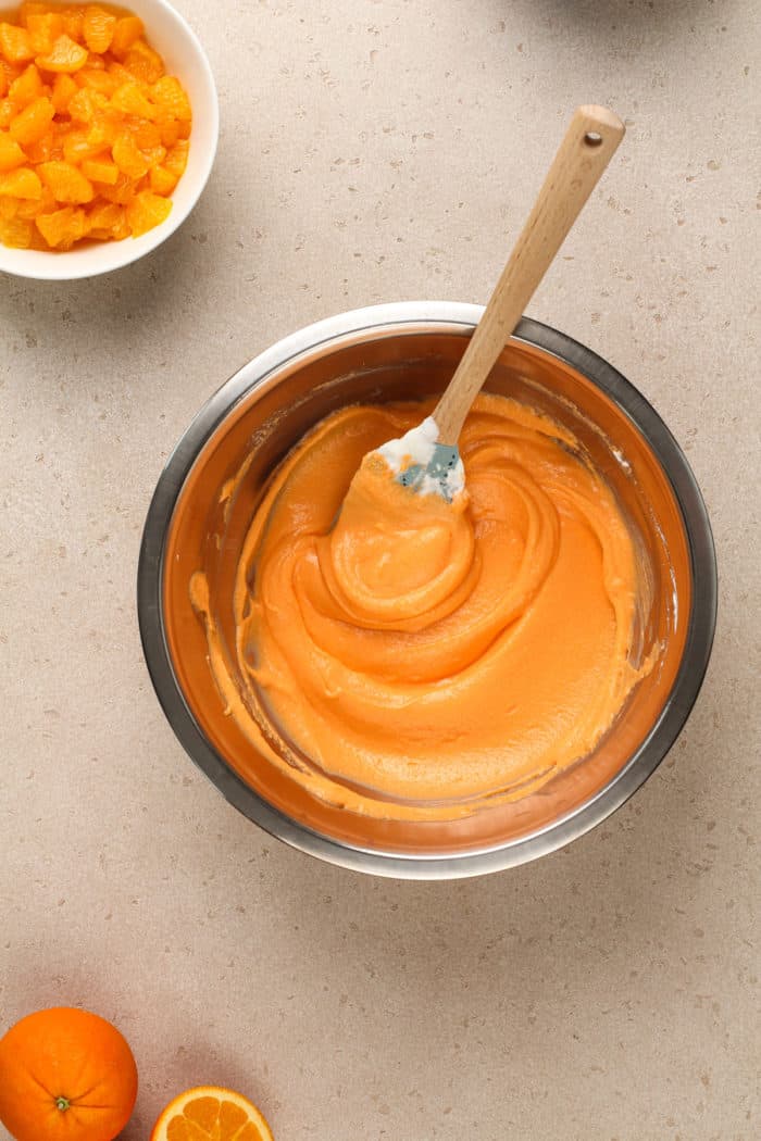 Orange jello mixed with pureed cottage cheese in a metal mixing bowl.