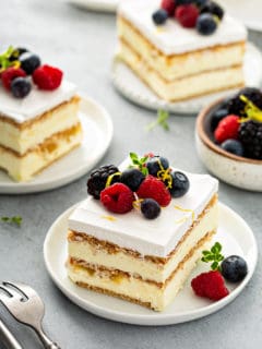 Three slices of lemon icebox cake on white plates, arranged on a gray countertop