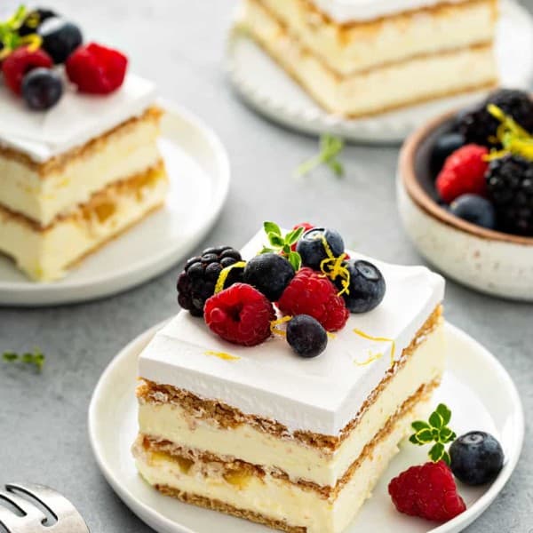 Three slices of lemon icebox cake on white plates, arranged on a gray countertop