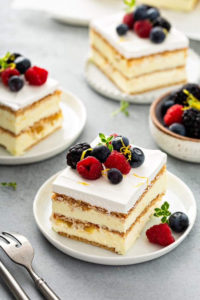 Three slices of lemon icebox cake on white plates, arranged on a gray countertop