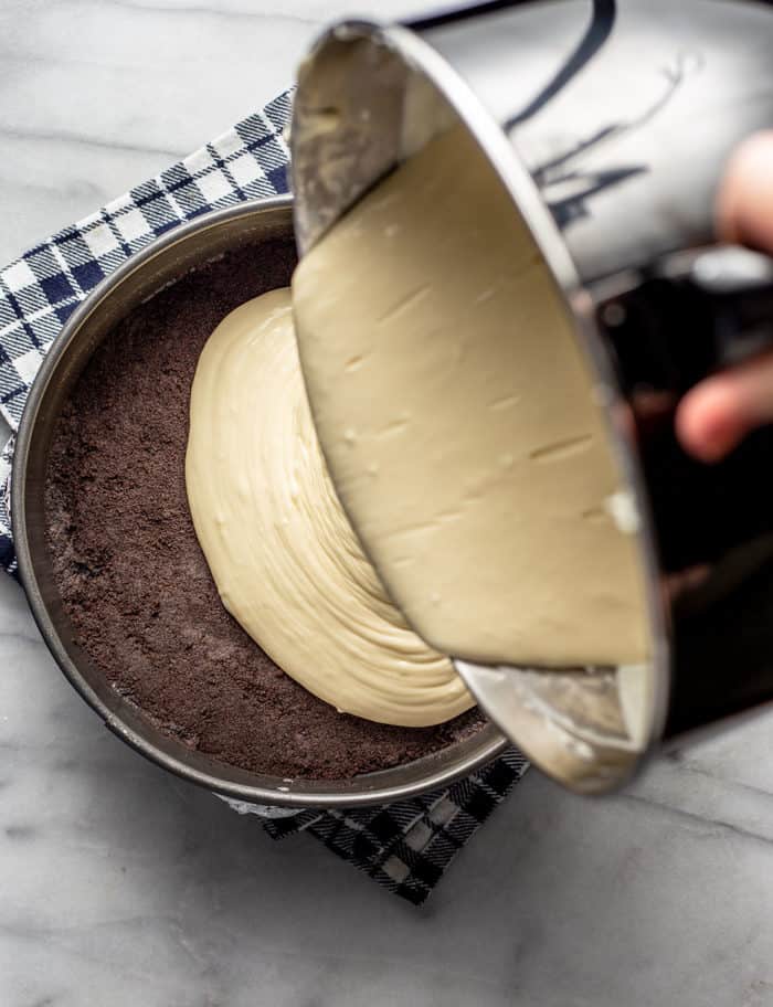 Baileys cheesecake filling batter being poured onto an Oreo cookie crust in a springform pan