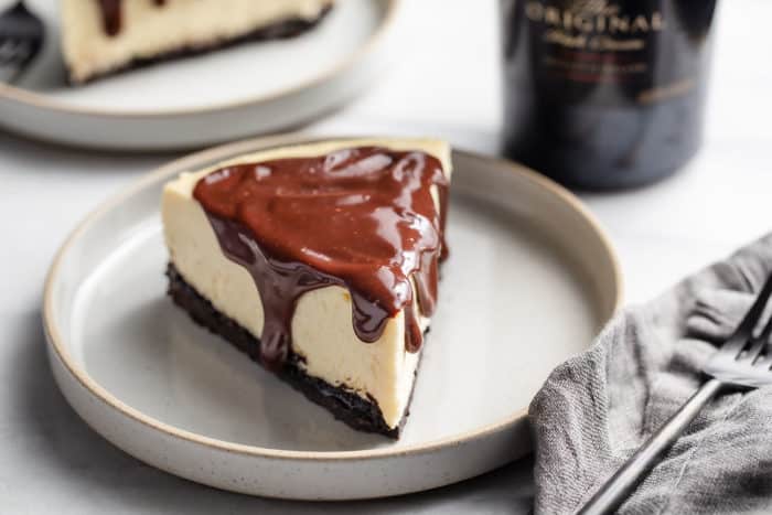 Slice of Baileys cheesecake topped with Baileys-spiked ganache on a gray plate