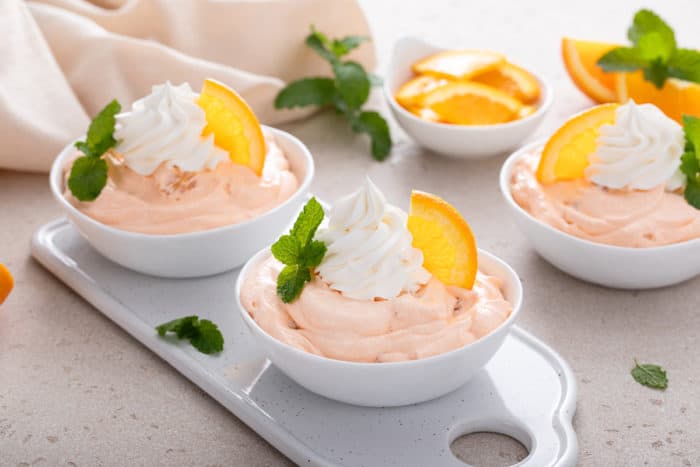 Three small white bowls filled with orange fluff and garnished with whipped cream and fresh orange slices.