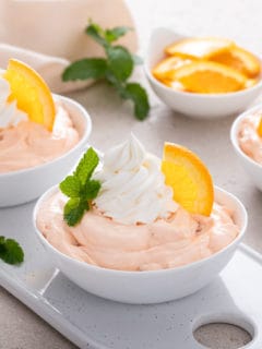 Bowls filled with orange fluff and garnished with whipped cream and orange slices.