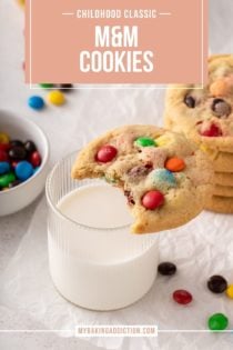 M&M cookie with a bite taken out of it set on the edge of a glass of milk. Text overlay includes recipe name.