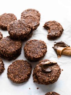 No bake cookies on a white surface next to peanut butter and melted chocolate