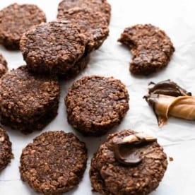 No bake cookies on a white surface next to peanut butter and melted chocolate