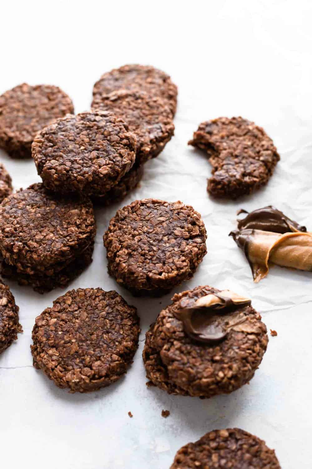 No bake cookies on a white surface next to peanut butter and melted chocolate