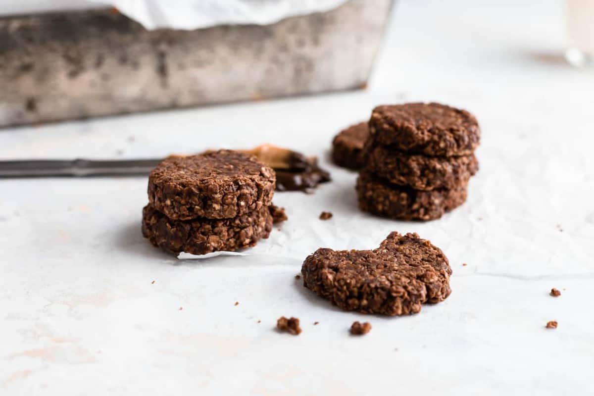 Chocolate no bake cookies on a white surface, one with a bite taken out of it