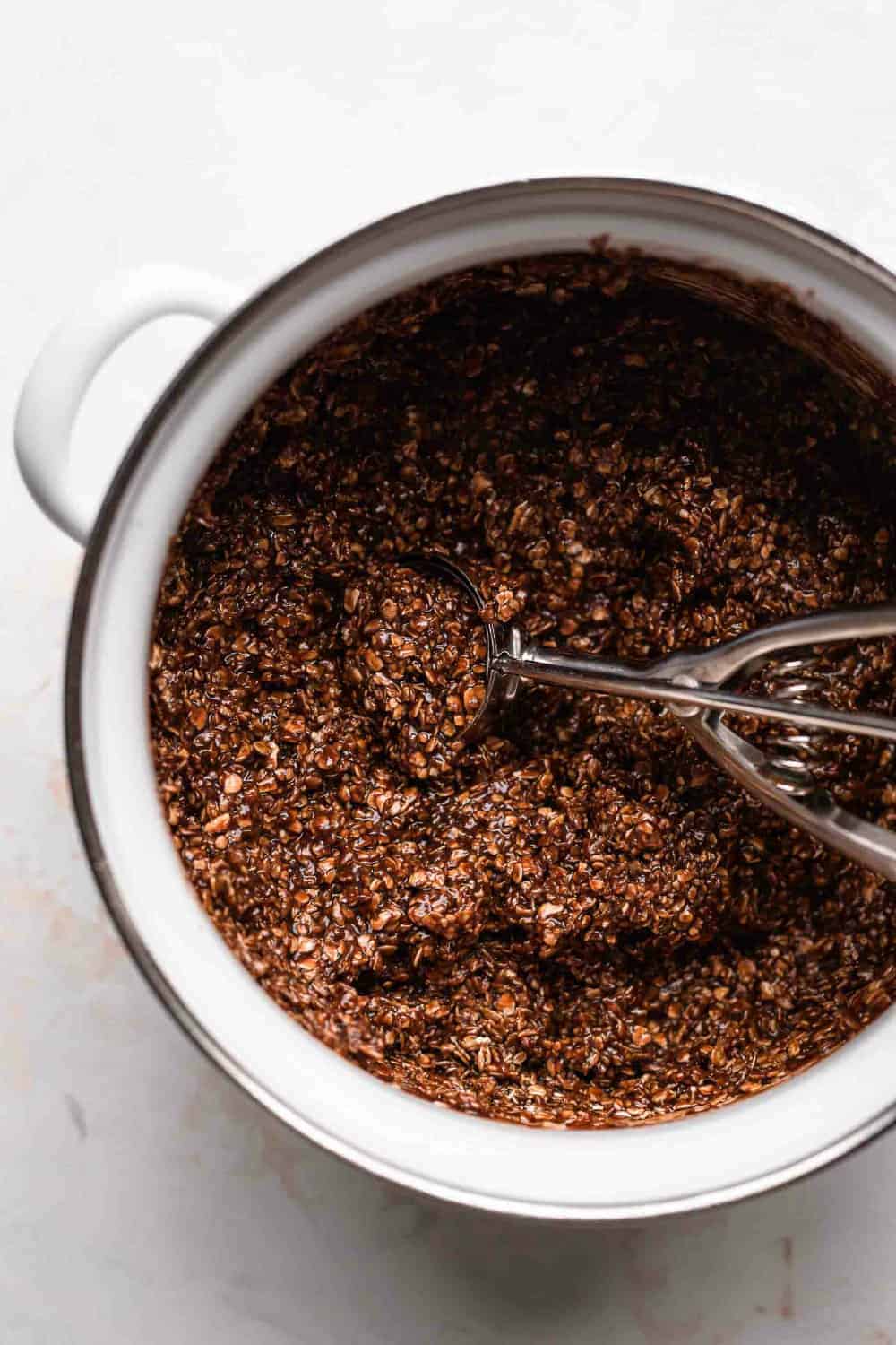 Chocolate, peanut butter and oat mixture for no bake cookies in a white sauce pot with a cookie scoop