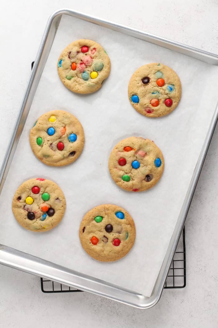 6 baked m&m cookies on a parchment-lined baking sheet.